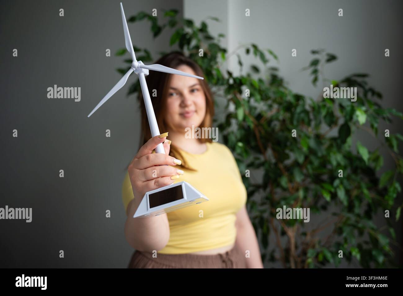 Junge Frau hält ein kleines Modell-Windrad in einem hellen Innenraum. Nachhaltigkeitserziehung, erneuerbare Energien und Eco-Startup-Konzepte. Stockfoto
