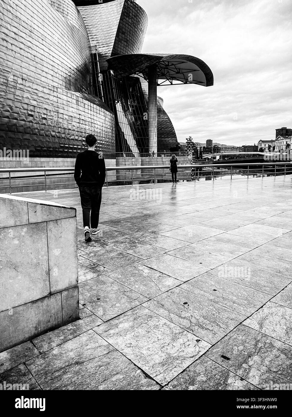 Schwarzweiß-Architekturansicht eines Besuchers, der neben dem Guggenheim Museum Bilbao spaziert, entworfen von Frank Gehry, Bilbao, Spanien. Stockfoto