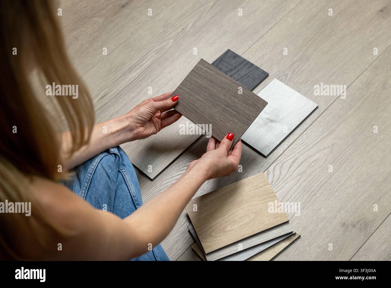 Frau sitzt auf dem Boden und wählt Holzfußbodenproben für die Hausrenovierung und Inneneinrichtung Stockfoto