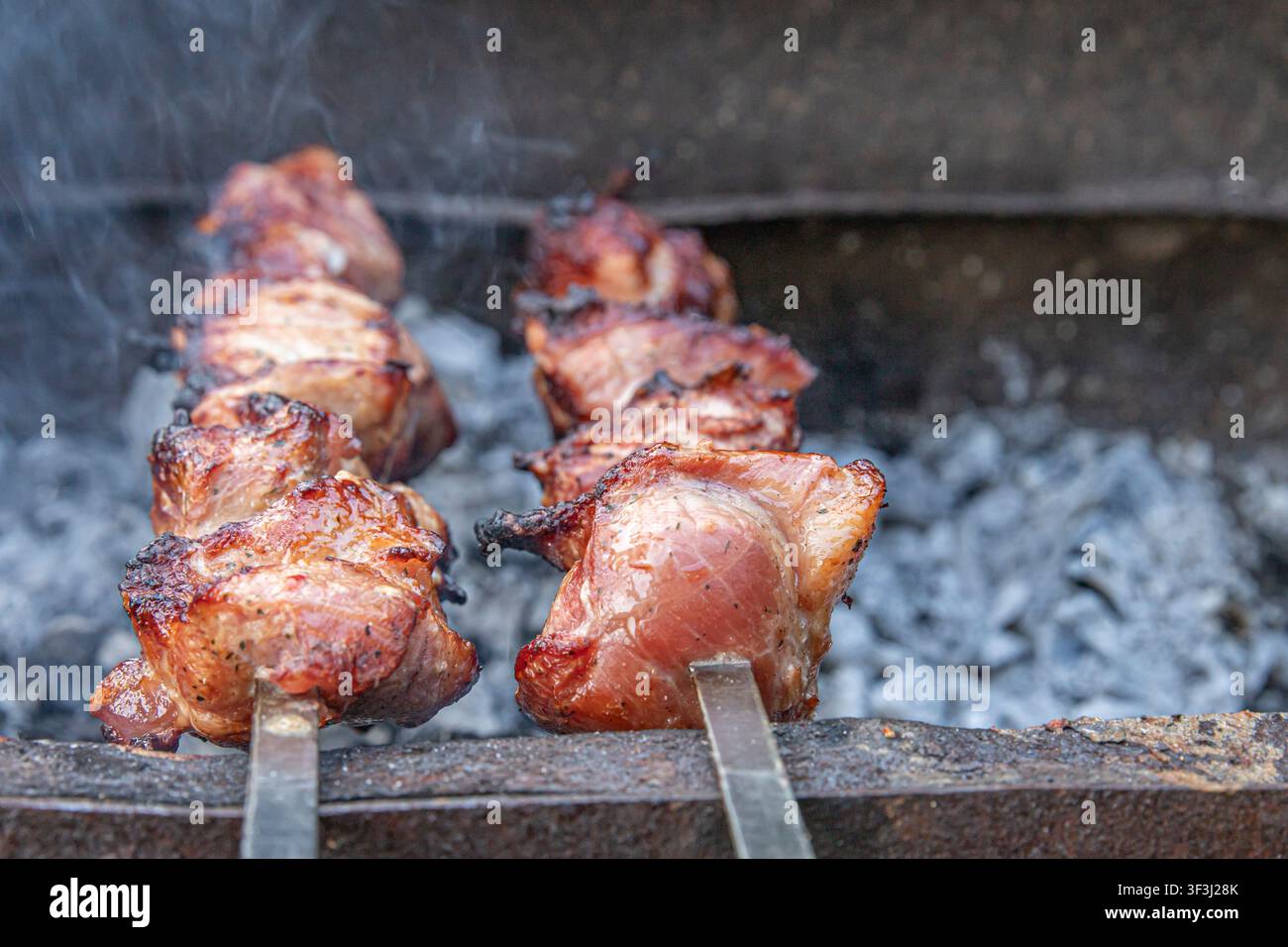 Saftige gegrillte Schweinespieße, die über heißer Holzkohle mit aromatischem Rauch im Freien gegart werden Stockfoto