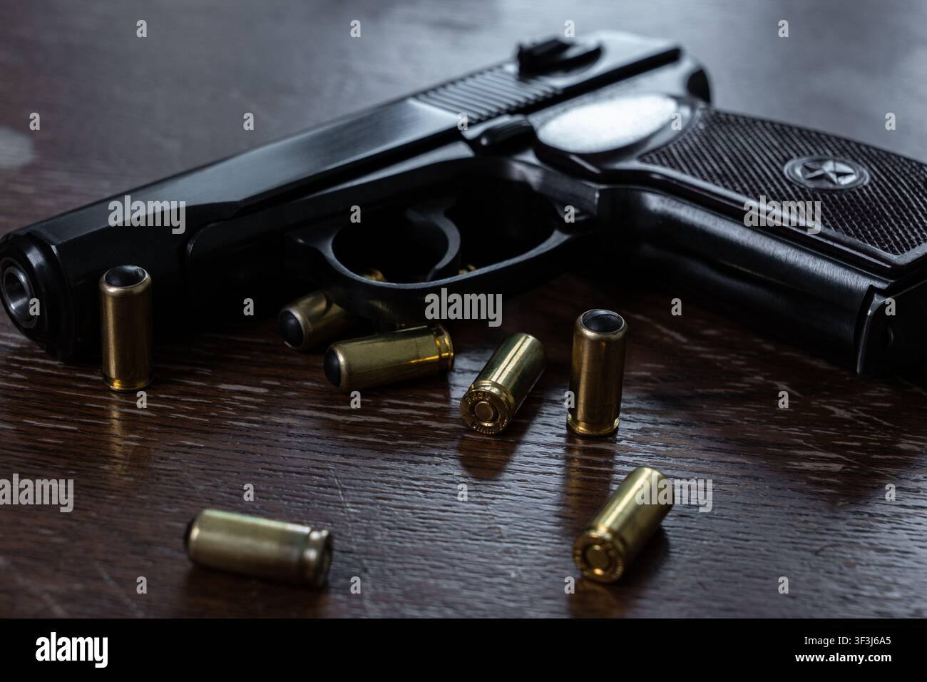 Schwarze Handfeuerwaffe, die auf einer dunklen, texturierten Holzoberfläche liegt, mit verstreuten nichtletalen Munitionshülsen, die schwarze Gummigeschosse enthalten. Stockfoto