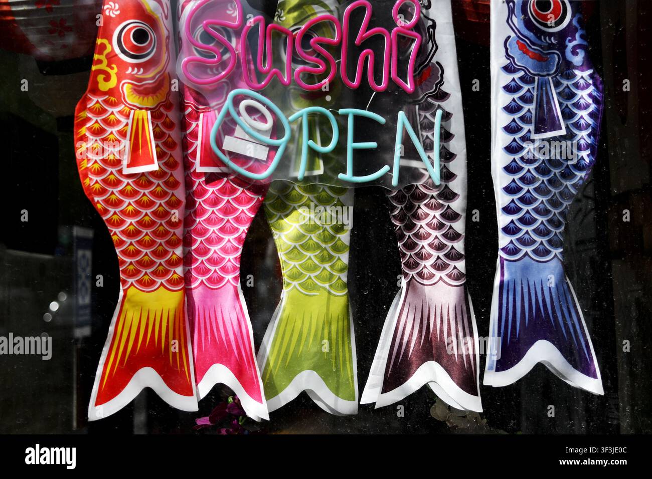 farbige Koinobori (traditionelle japanische Karpfenwimpel) hängen in einem Schaufenster neben einem „OPEN“-Neonschild in Montmartre - Paris - Frankreich Stockfoto