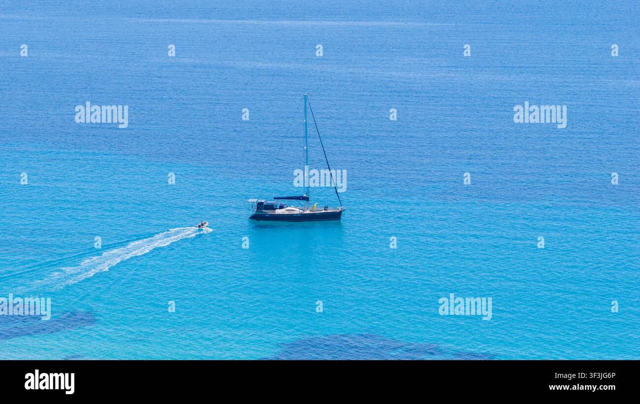 Possidi Beach, Griechenland, 11. Juli 2026. Ein Segelboot ruht auf dem klaren türkisfarbenen Wasser des Possidi-Strandes in Griechenland, während ein Jetski in der Nähe eine Spur hinterlässt an einem s Stockfoto