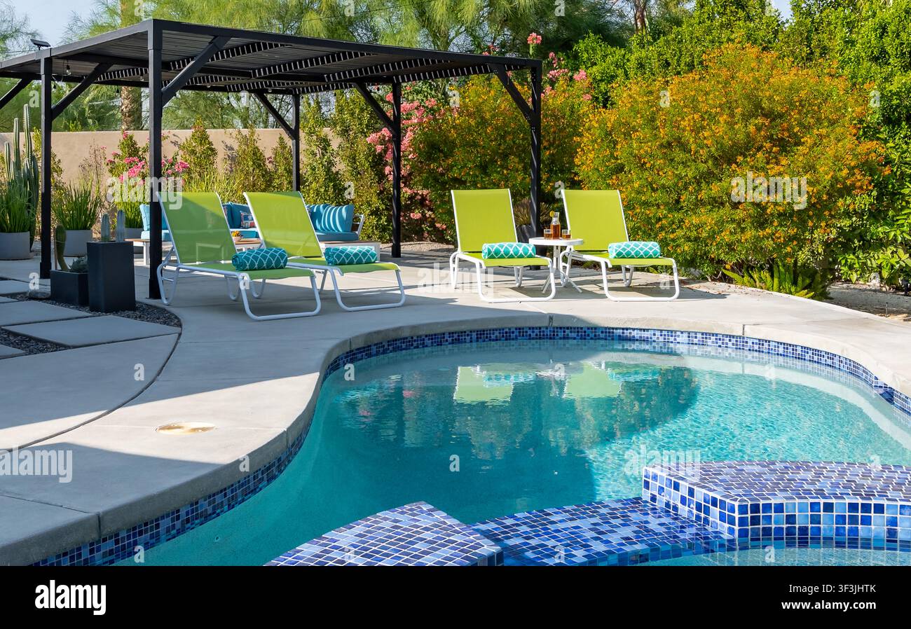 Poolbereich mit limettengrünen Patio-Liegestühlen, üppiger Vegetation und Wüstenlandschaft. Stockfoto
