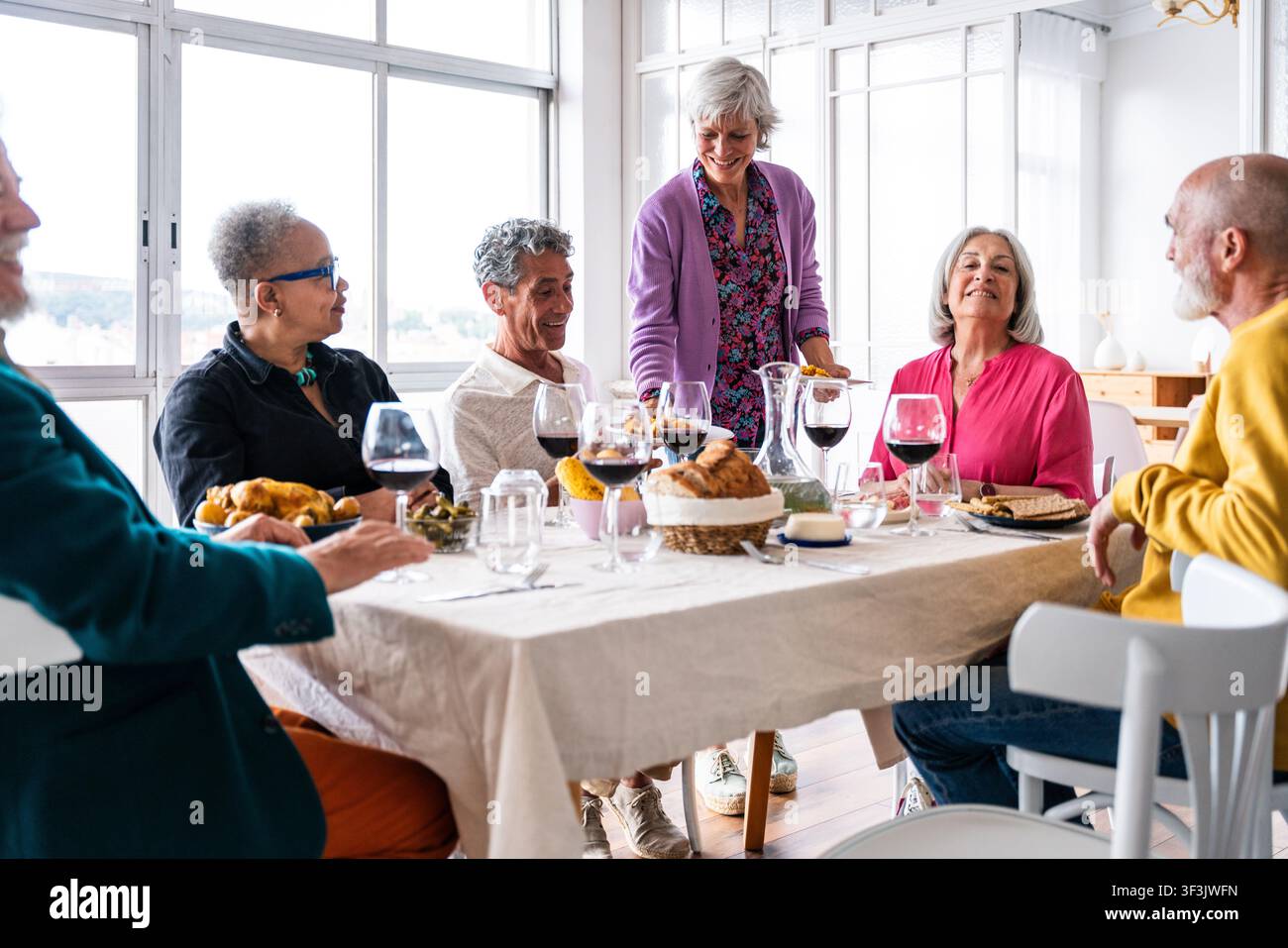 Senior-Freunde, die gemeinsam eine fröhliche Mahlzeit an einem Esstisch genießen, einen intimen Moment der Freundschaft und Gemeinschaft über Essen und Wein Stockfoto
