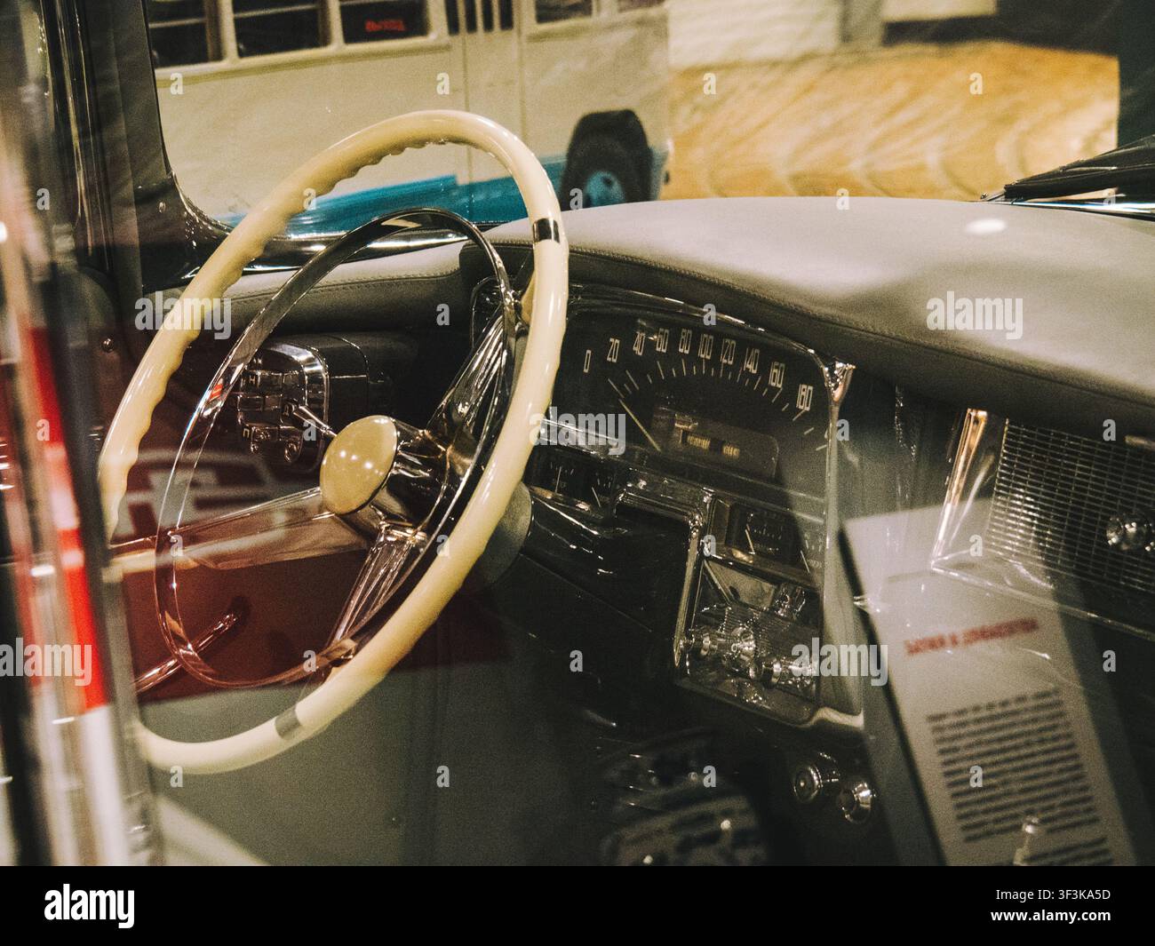 Vintage-Armaturenbrett aus den 1950er Jahren mit cremefarbenem Lenkrad, Chromverzierungen und analogem Geschwindigkeitsmesser in einem klassischen Automuseum. Stockfoto