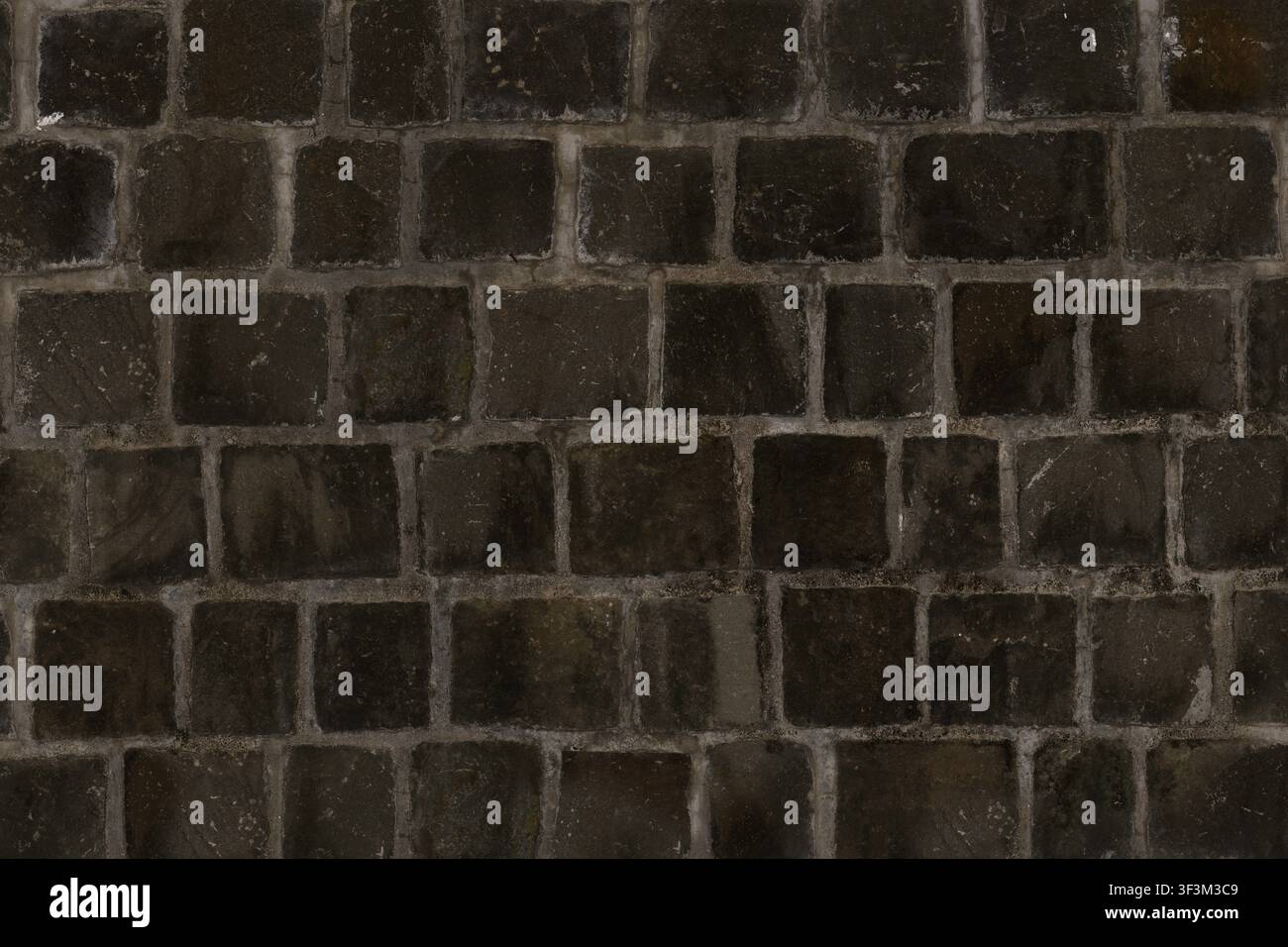 Eine Wand aus dunklen kohleschwarzen quadratischen Steinblöcken, die einen einheitlichen und modernen architektonischen Look erzeugen. Stockfoto