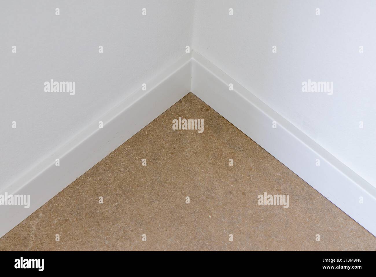 Ein minimalistisches Innendetail, das den Übergang eines strukturierten Bodens und glatter weißer Wände mit Sockelleiste zeigt Stockfoto