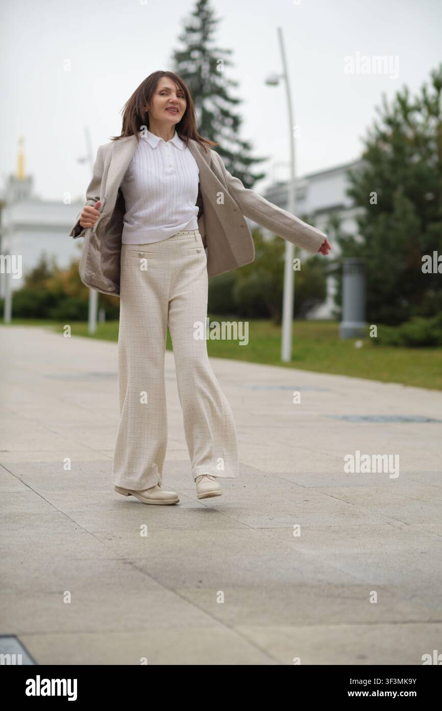 Eine reife Frau geht mit Flair, halb tanzt auf einem öffentlichen Weg. Dieses Lifestyle-Foto zeigt, dass Selbstvertrauen und spielerischer Geist nicht verblassen Stockfoto