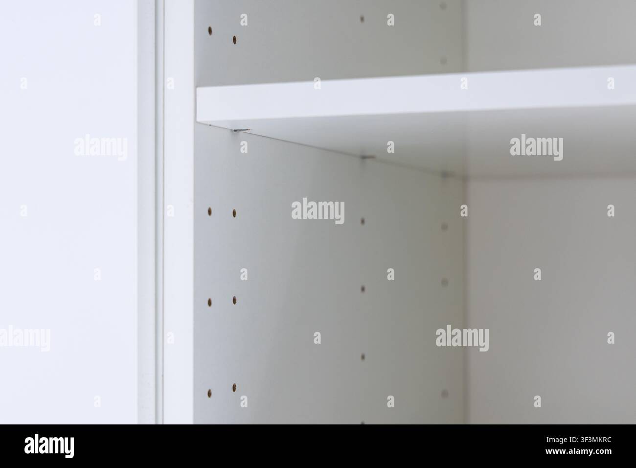 Das Innere einer modernen weißen Regalunit zeigt präzise vorgebohrte Löcher für die Regalplatzierung und subtile Metallstifte, die ein Regal unterstützen Stockfoto