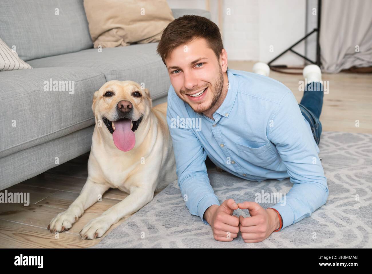 Junger glücklicher Kerl, der mit seinem Hund auf dem Boden liegt Stockfoto