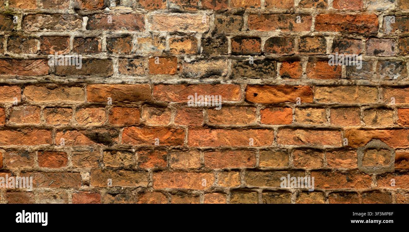 Eine alte, verwitterte rote Backsteinmauer mit Resten von Mörtel und Pflasterflickarbeiten, die eine rustikale, antike Qualität aufweist. Stockfoto