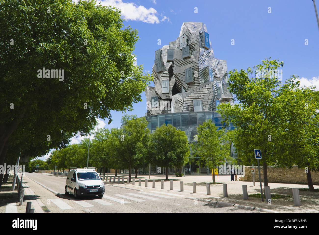Ein Lieferwagen fährt auf einer Straße an dem auffälligen modernen Wahrzeichen des LUMA-Turms vorbei, der von Frank Gehry in Arles, Frankreich, entworfen wurde. Stockfoto