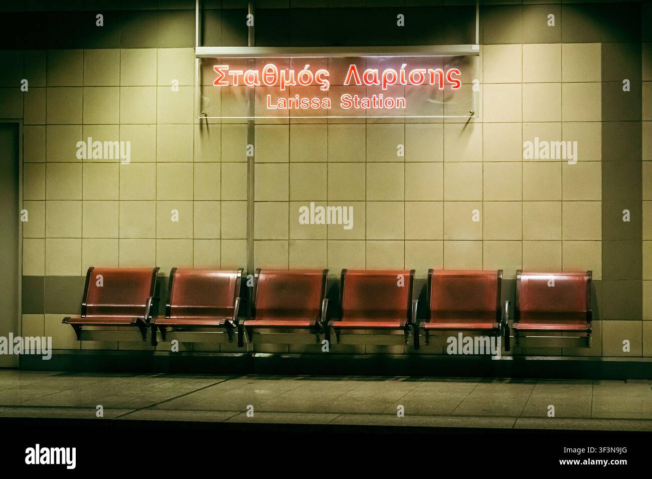 Wartebereich des Bahnhofs Larissa (Stathmos Larisis), Zentralbahnhof in Athen, Griechenland. Leere rote Sitze unter einem leuchtenden zweisprachigen Neonschild bei Stockfoto