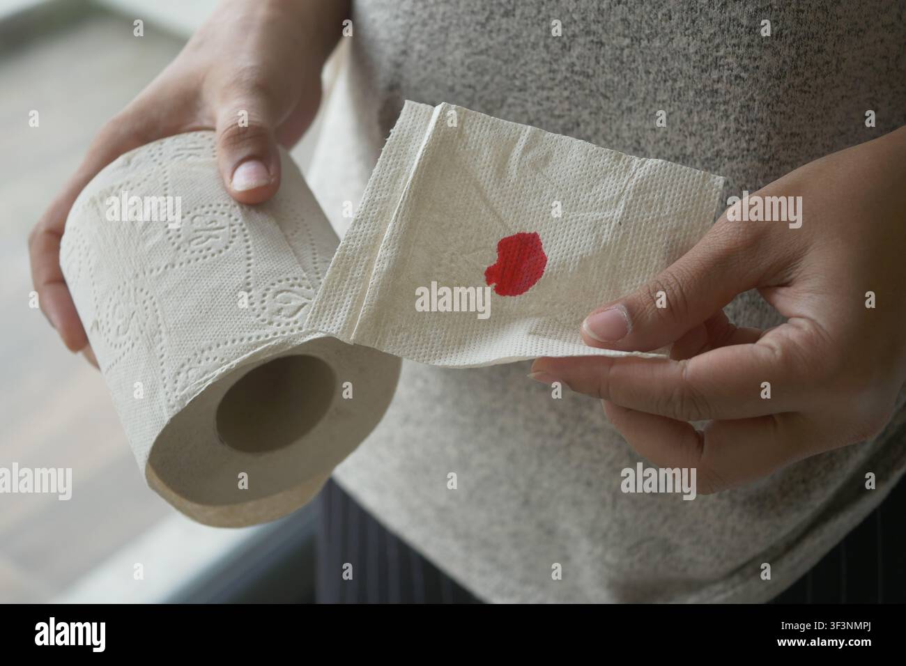 Frau hält Toilettenpapier mit rotem Fleck in einer häuslichen Umgebung Stockfoto
