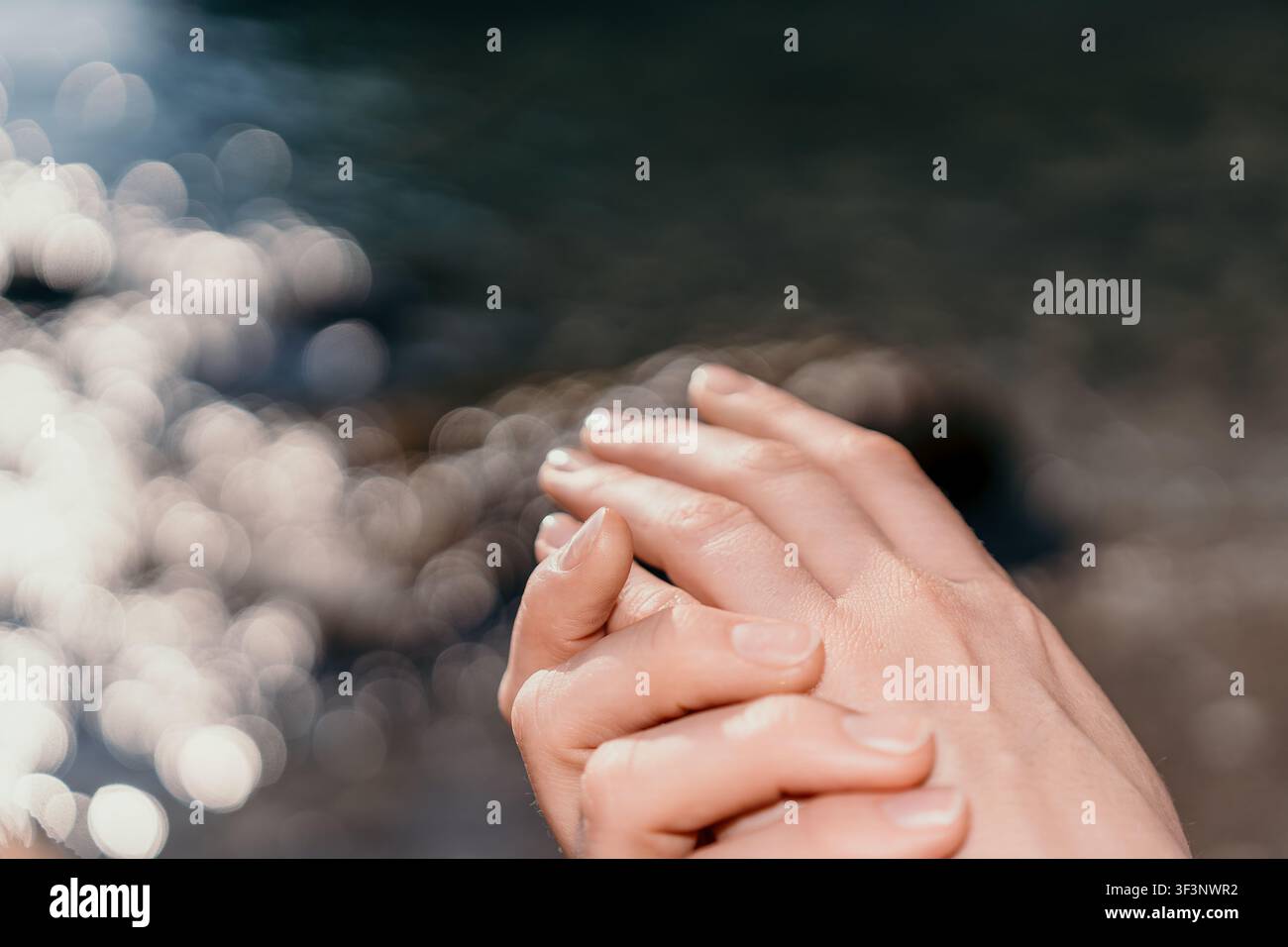 Nahaufnahme von weiblichen Händen, die sich sanft in der Nähe von glitzernden Wellen am Strand während eines friedlichen Sonnenuntergangs befinden Stockfoto