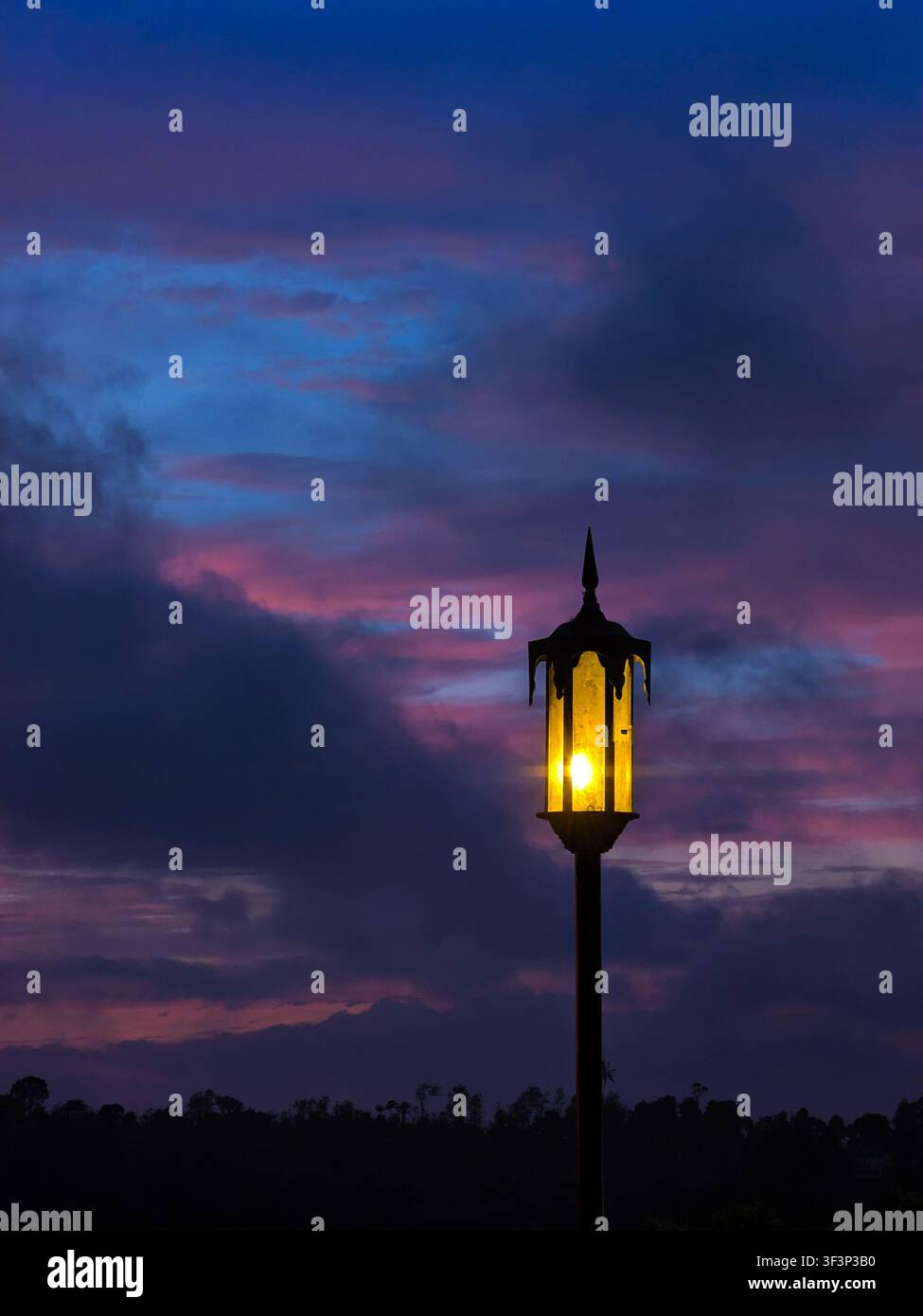 Leuchtende Vintage-Straßenlaterne vor einem dramatischen dunkelblauen und violetten Abenddämmerungshimmel - Smartphone-aufgenommenes Stockfoto