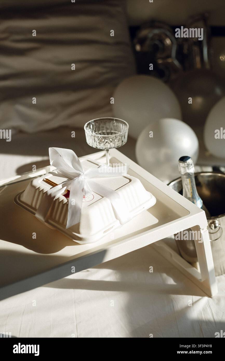 Verpackter und dekorierter Kuchen mit Champagnerflasche und Ballons auf einem Tablett bei Sonnenlicht Stockfoto