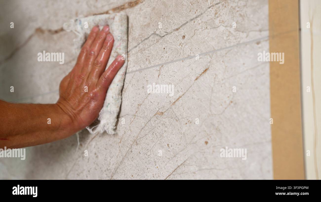 Hand poliert eine Marmoroberfläche mit einem Tuch. Ein Arbeiter wischt Keramikfliesen nach dem Verfugen mit Epoxidfuge ab. Stockfoto