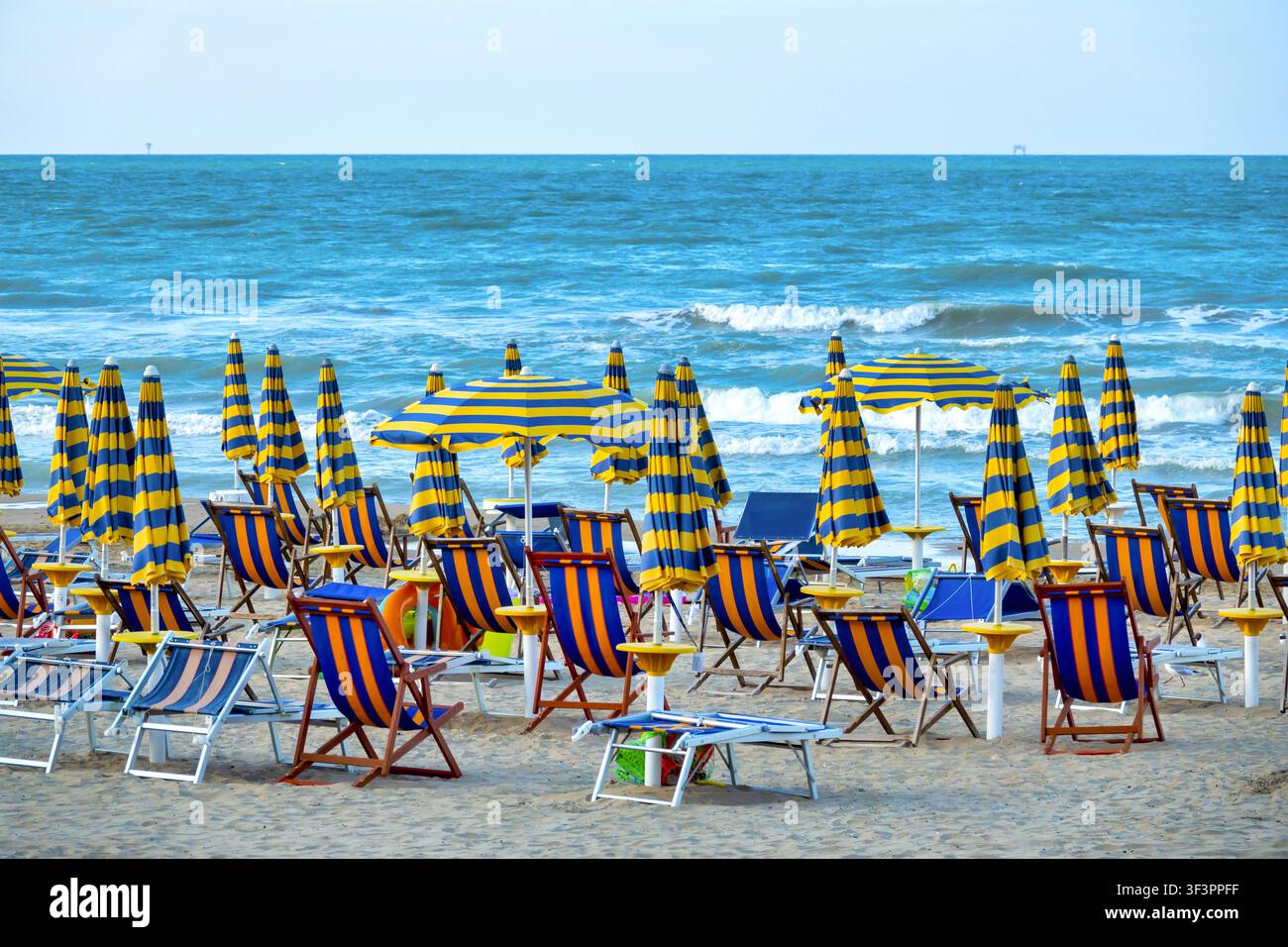 Leerer Strand mit blau-gelb gestreiften Sonnenschirmen und Liegestühlen, die dem Meer zugewandt sind. Italienische Küste, Adriatisches Meer. Stockfoto