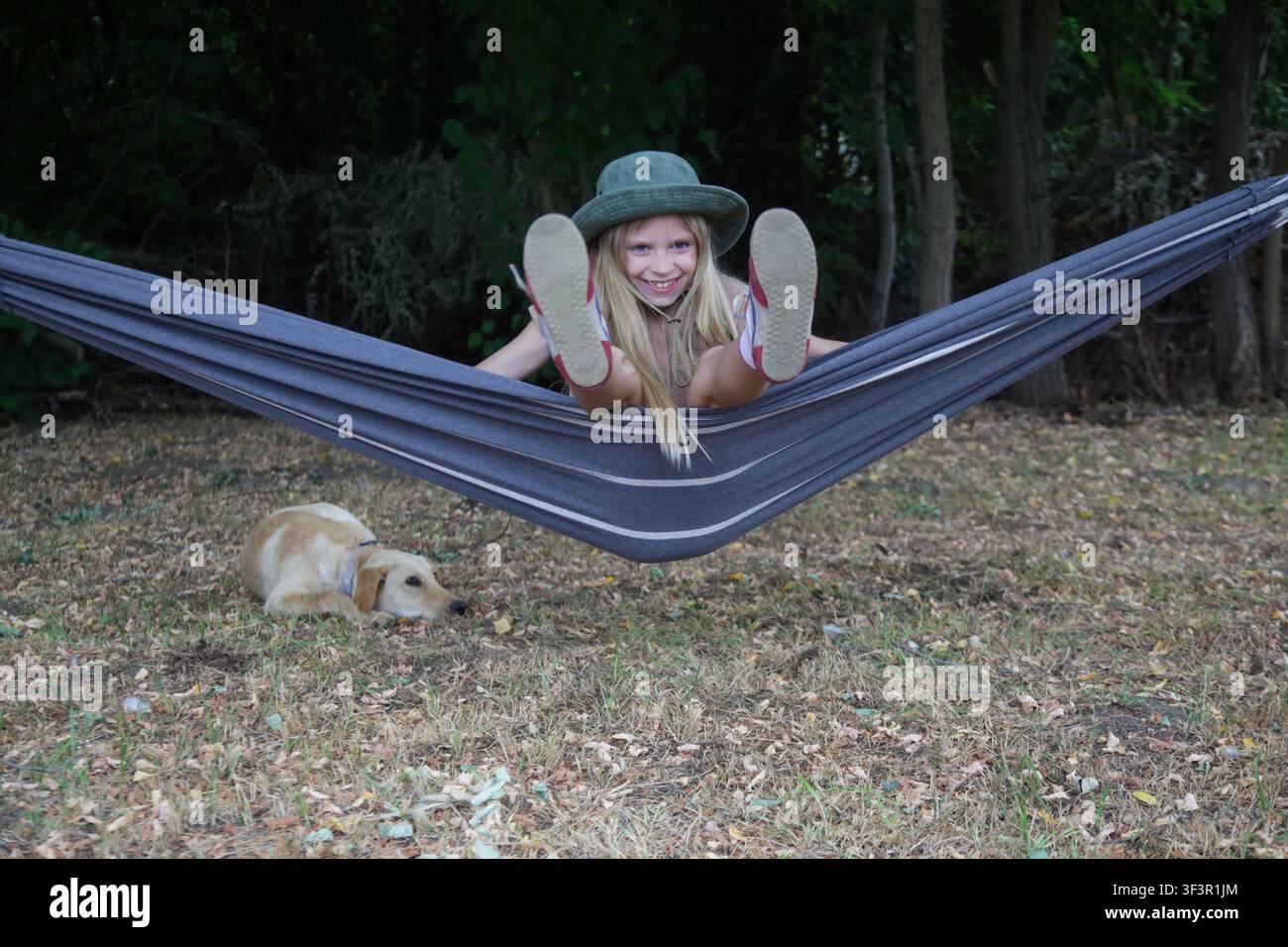 Glückliches Mädchen genießt einen unbeschwerten Kindheitsmoment beim Camping in der Hängematte mit dem Hund Stockfoto