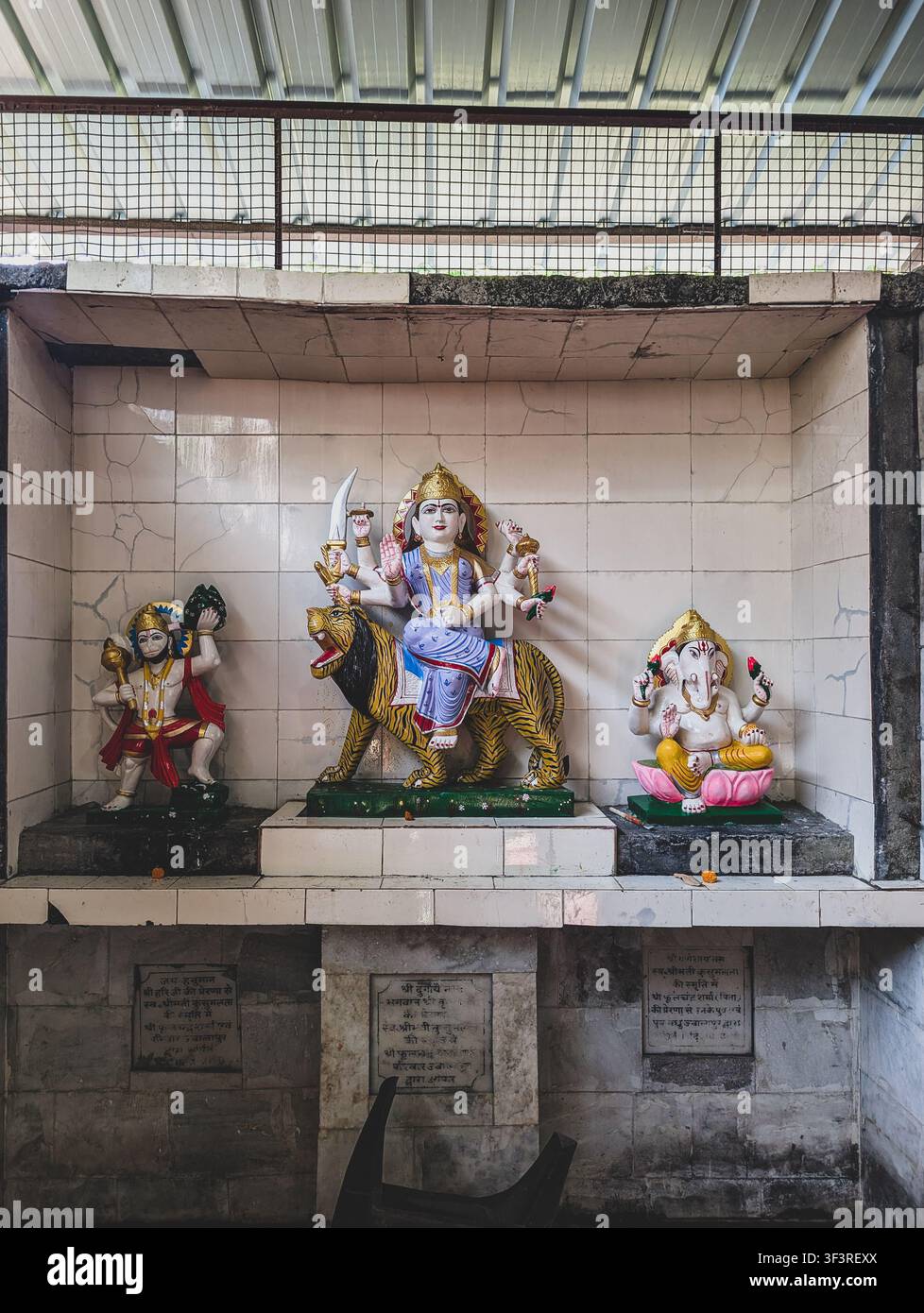 Hinduistischer Tempelschrein mit bunten Götzenstatuen, darunter Durga auf einem Tiger und Ganesha, ausgestellt in einer kleinen gefliesten Nische. Stockfoto