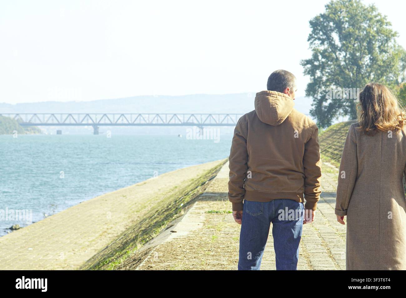 Paar geht unter weichem Licht entlang der Uferpromenade weg. Geht gemeinsam vorwärts und Partnerschaft, die durch alltägliche Beständigkeit aufgebaut wird. Stockfoto