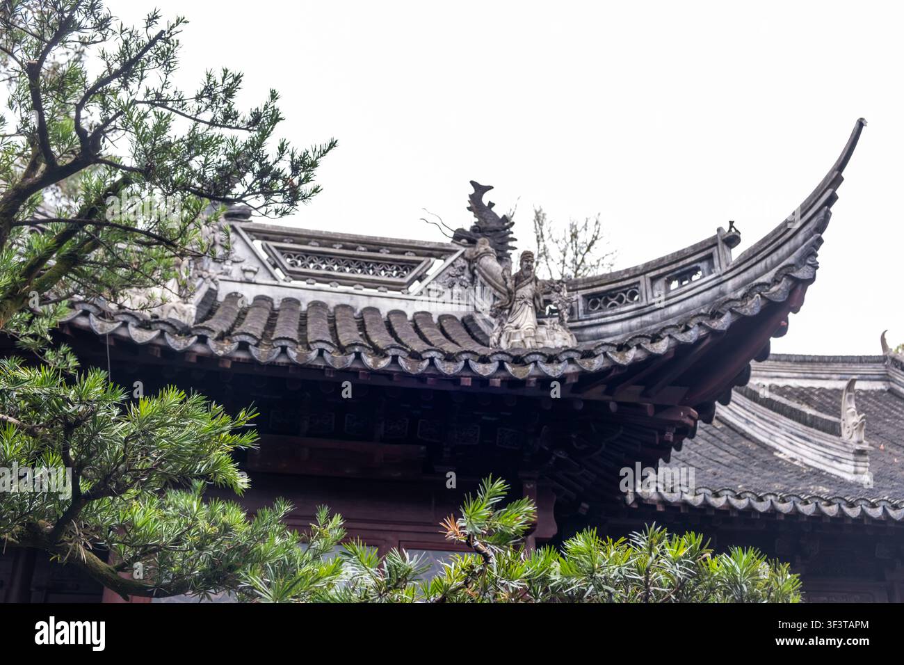 Gekrümmtes Ziegeldach mit geschnitzten Figuren und Kiefernzweigen im Jade-Buddha-Tempel in Shanghai, China, an einem Frühlingstag Stockfoto
