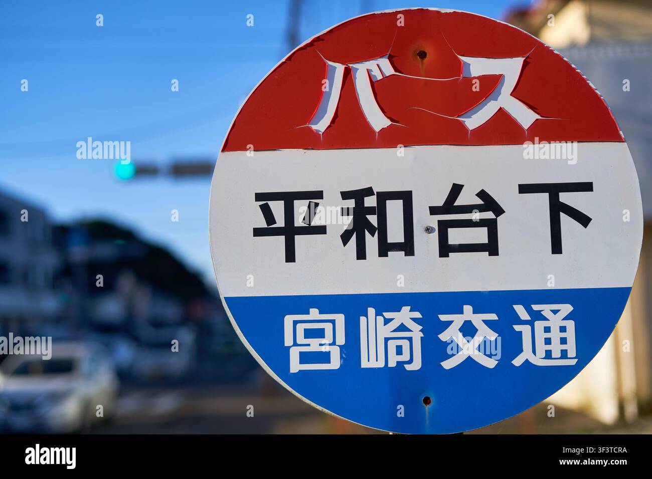 Eine Nahaufnahme eines runden japanischen Bushaltestellenschilds, das an einem Pfosten montiert ist, vor einem städtischen Straßenhintergrund mit Bokeh-Effekt. Das Schild zeigt Stockfoto