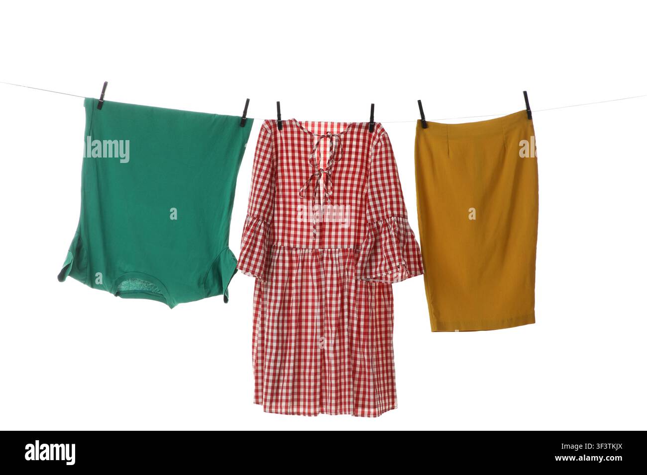 Grünes T-Shirt, rotes Gingham-Kleid und gelber Rock, die mit Wäscheklammern an einer Wäscheleine hängen, isoliert Stockfoto