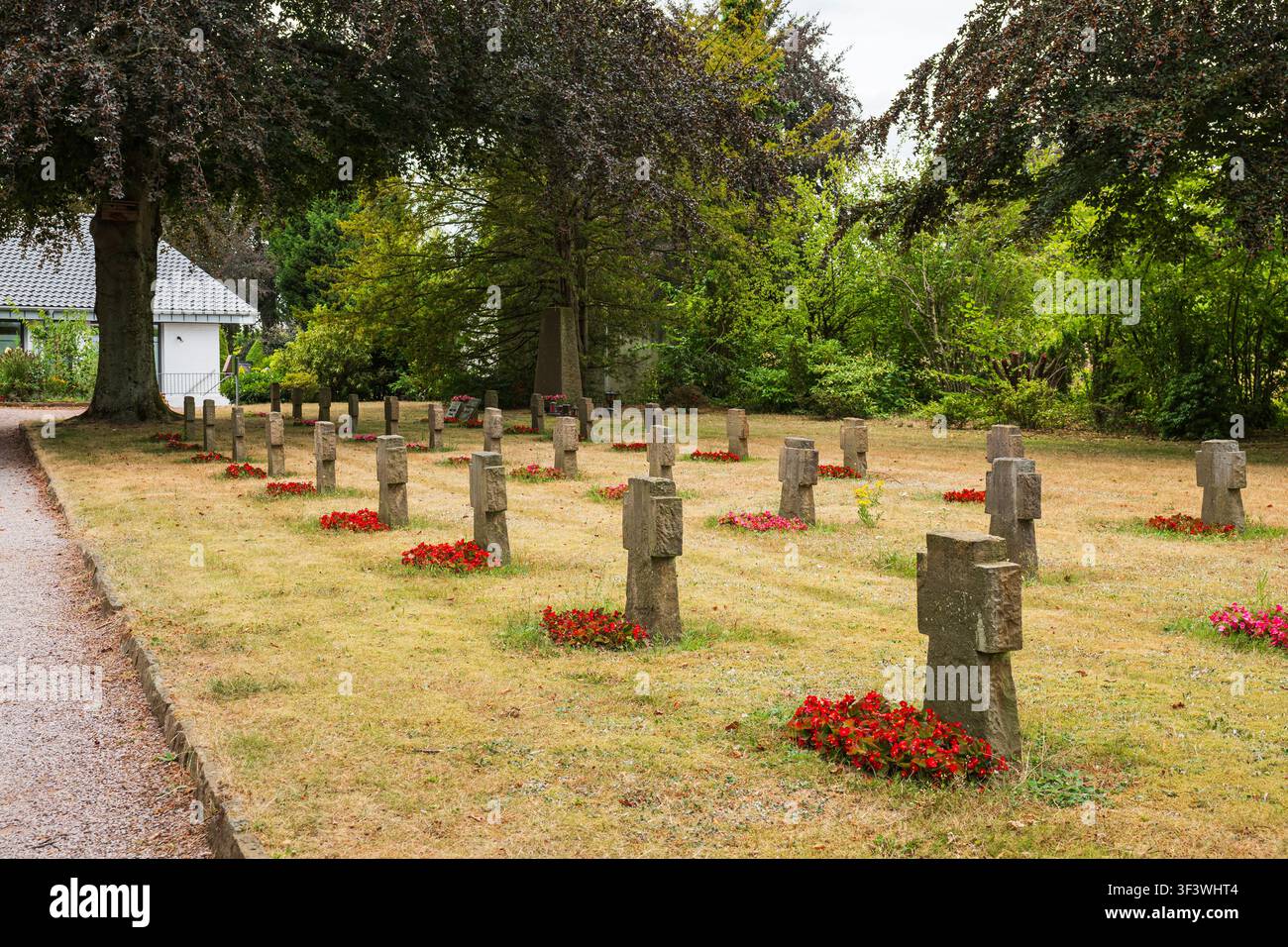 Militärfriedhof mit steinernen Kreuzen und roten Blumenbeeten in einer friedlichen Sommerparklandschaft Stockfoto