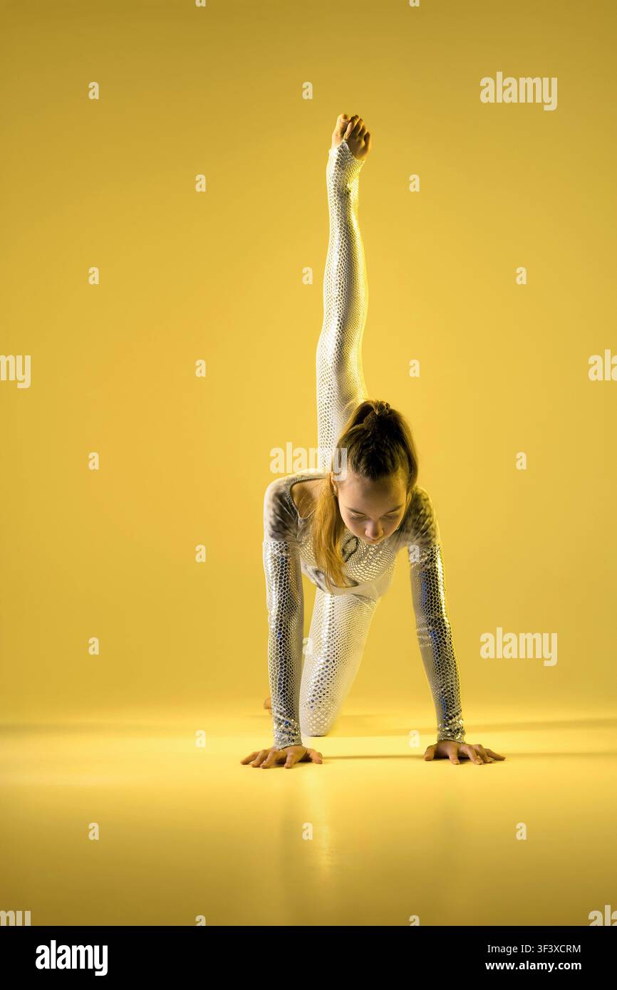Turner führt eine Spagat-Pose auf einem gelben Hintergrund aus. Konzept: Werbung für Sportschulen, Tanzstudios, Innendekorationsdrucke und Fitness-Apps Stockfoto