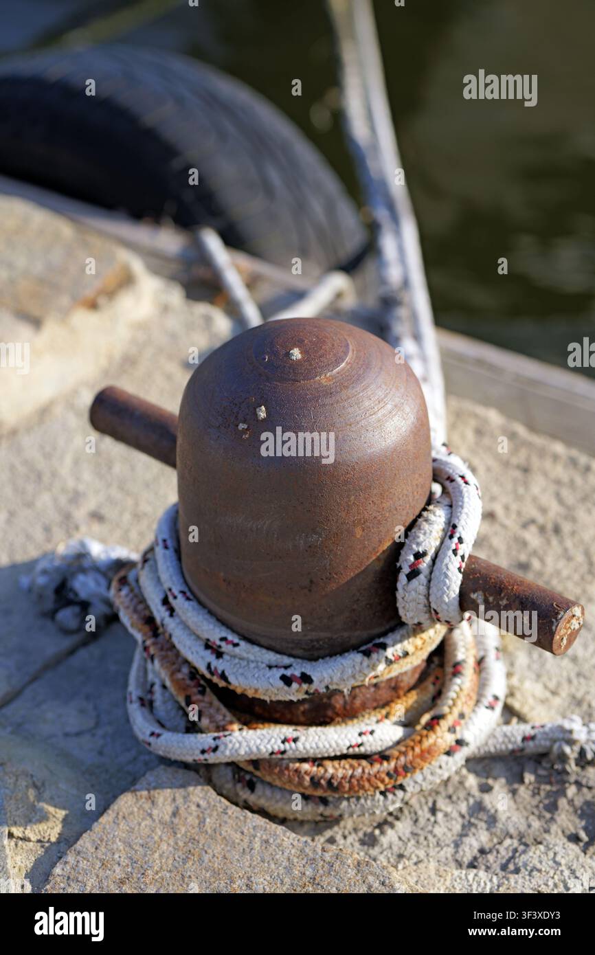 Rostige Gusseisen-Pfahl sichert ein dickes Ankertau und bietet einen starken Punkt zum Festmachen von Booten und Schiffen in einem geschäftigen Hafen Stockfoto