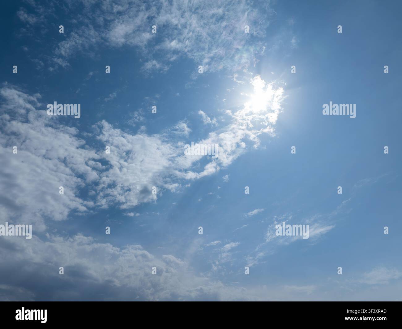 Weiter blauer Himmel gefüllt mit verschiedenen Wolken, von wolkig bis dicht. Die helle Sonne scheint von oben rechts und erzeugt Sonnenstrahleneffekte und erhellt die Stockfoto