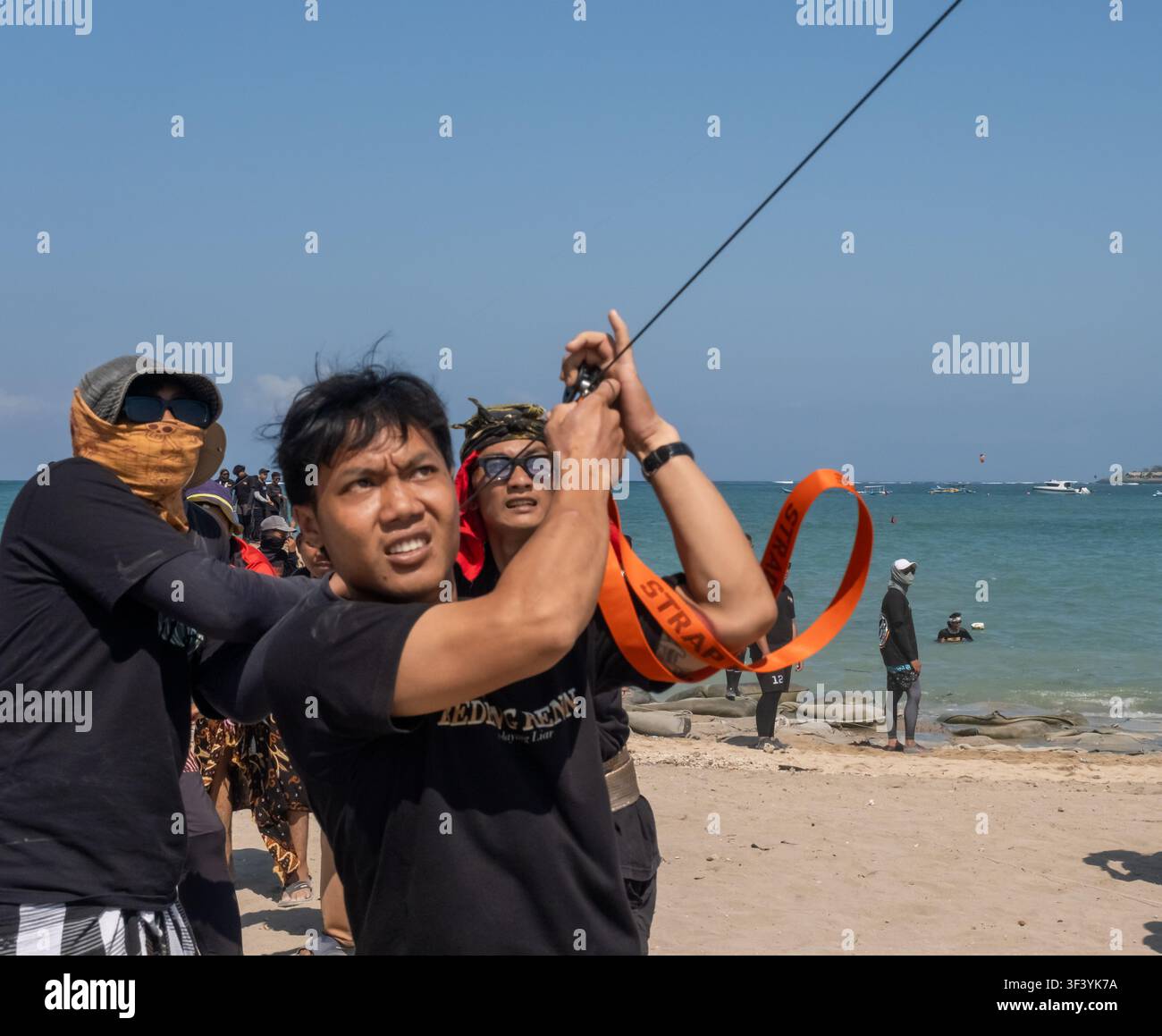 Junge balinesische Männer arbeiten zusammen, um ihre Drachen am Mertasari-Strand, Bali, Indonesien, am 18. Juli 2026 zu steuern. Stockfoto