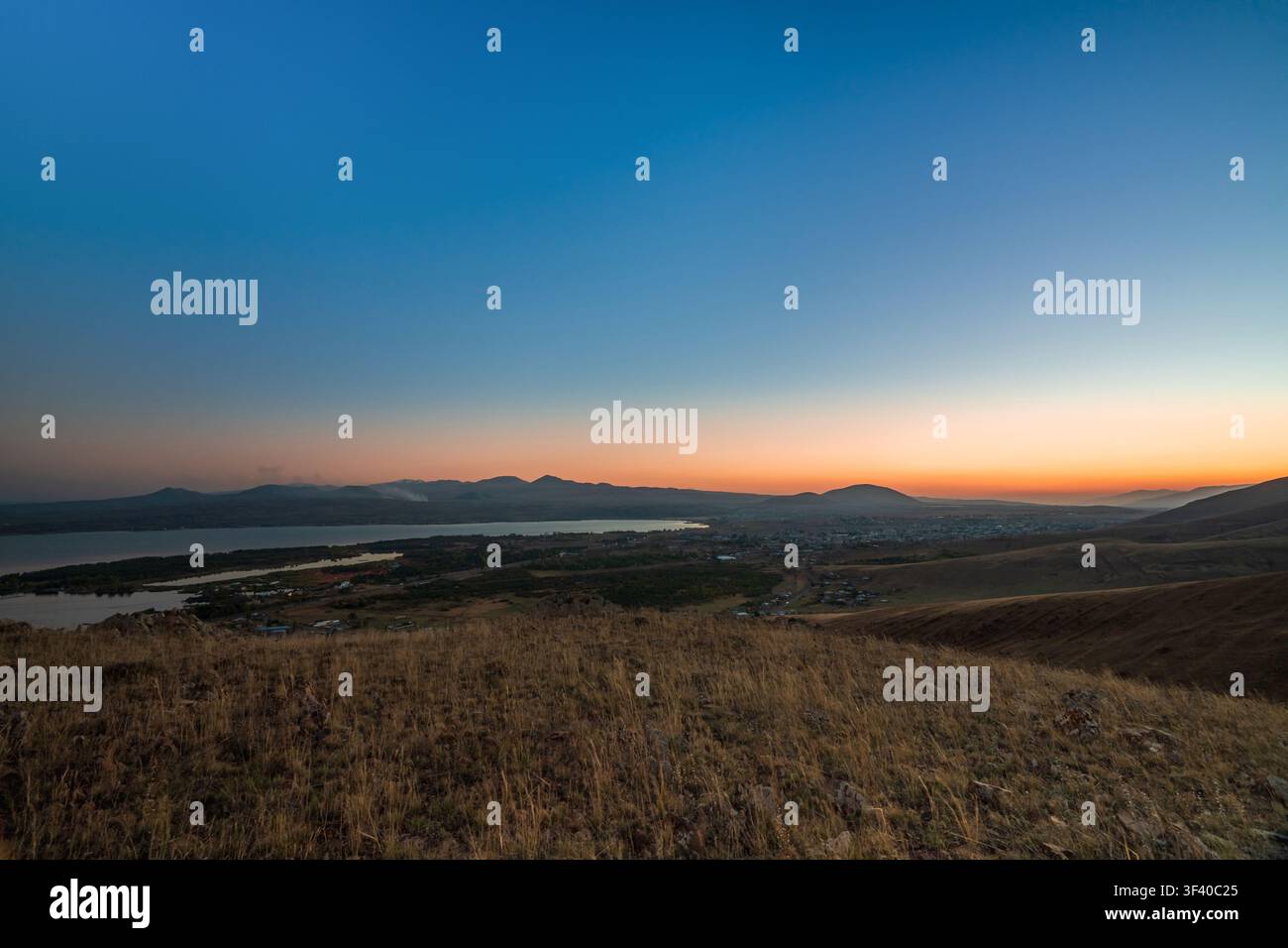 Ein atemberaubender Blick über das Sewan-Tal bei Sonnenuntergang, mit orangefarbenem Himmel, der oben über dem See in ein tiefes Blau übergeht, und den Silhouetten der Berge im Di Stockfoto