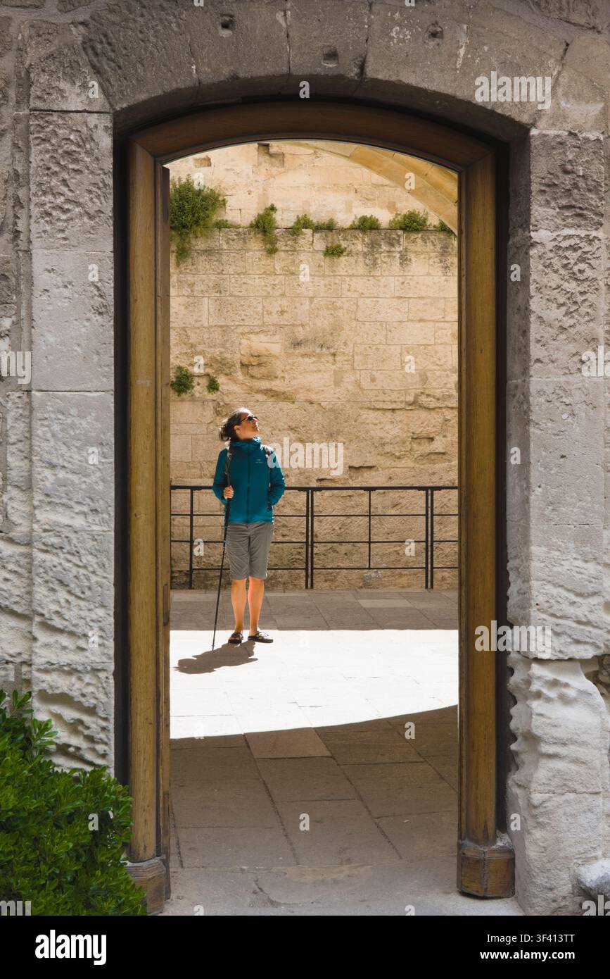 Ein Tourist, der von einem Steinbogen eingerahmt ist, erkundet historische Steinbauten im Château des Baux in Les Baux-de-Provence, Frankreich. Stockfoto