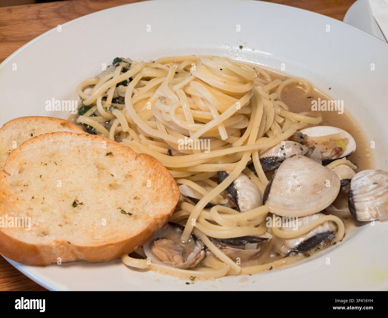 Eine Nahaufnahme von Spaghetti-Pasta gemischt mit Muscheln in einer cremigen Sauce, serviert mit gerösteten Knoblauchbrotscheiben in einer weißen Schüssel. Stockfoto