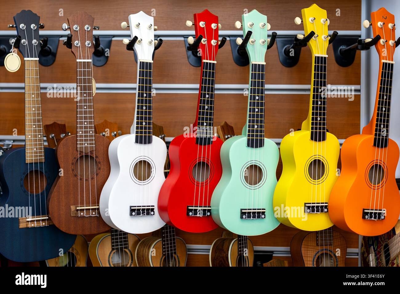 Bunte Ukulelen in einem Musikgeschäft ausgestellt. Eine bunte Reihe von Ukulelen hängt an einer hölzernen Musikgeschäftswand mit hellen Lackierungen und Saiten Stockfoto