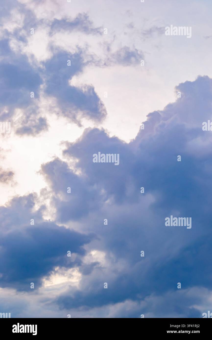 Eine vertikale Hintergrundfotografie, die dichte Kumulonimbuswolken zeigen, die nach einem schweren Donnersturm am Abendhimmel mit natürlichen violetten und purpurnen Tönen leuchten Stockfoto