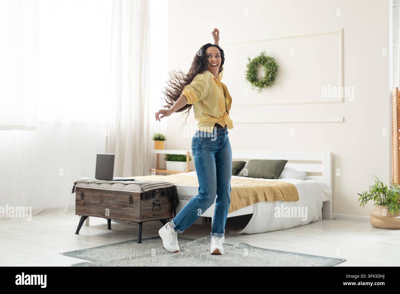 Glückliche junge Frau tanzt in einem gemütlichen Schlafzimmer, fröhliches Wohnkonzept Stockfoto