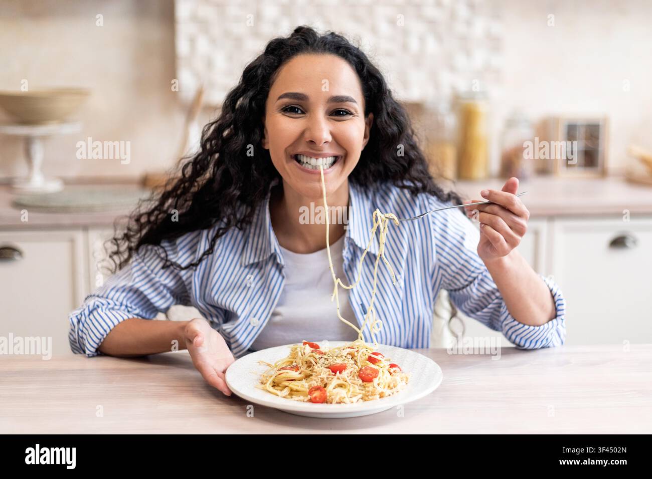 Lächelnde Frau isst Spaghetti in der Küche und genießt ein köstliches italienisches Gericht Stockfoto