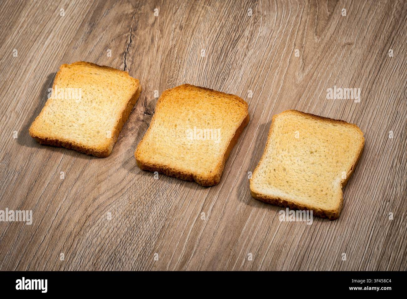 Drei knusprige Rusken auf einem hellbraunen Holztisch angeordnet, die ein einfaches Frühstück oder einen Snack präsentieren Stockfoto