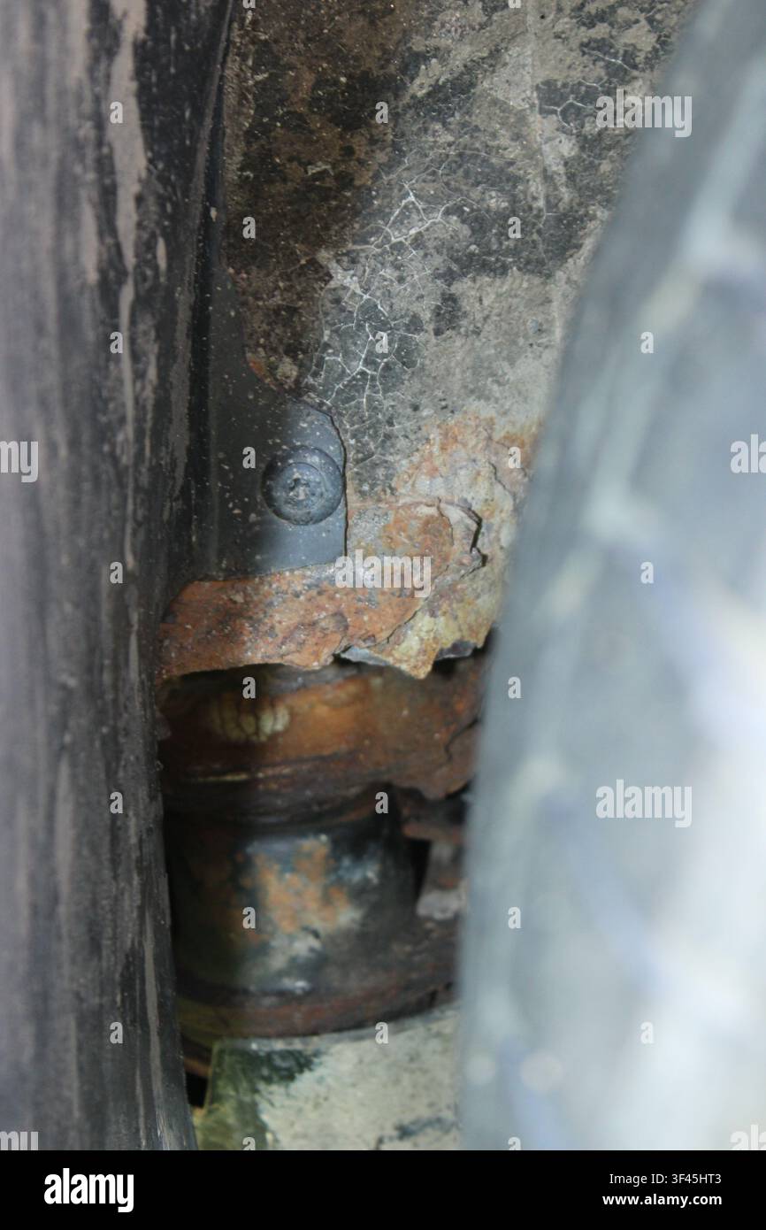 Rostiges, korrodiertes Metallaufhängungsteil in der Nähe eines Autorades und des Radkessels Stockfoto