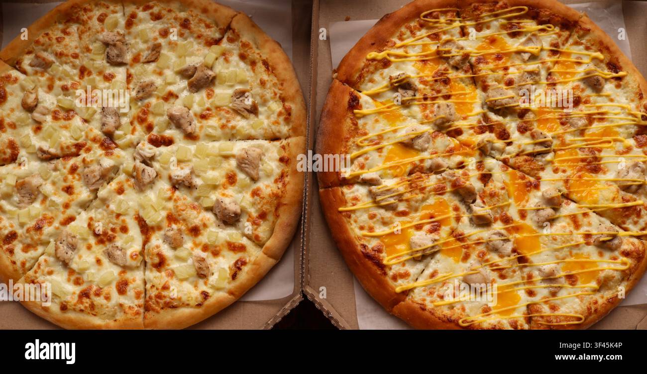 Zwei runde Pizzen in Kartons. Links ist eine klassische Hawaii-Pizza mit Hähnchen- und Ananasstücken auf Mozzarellakäse. Stockfoto