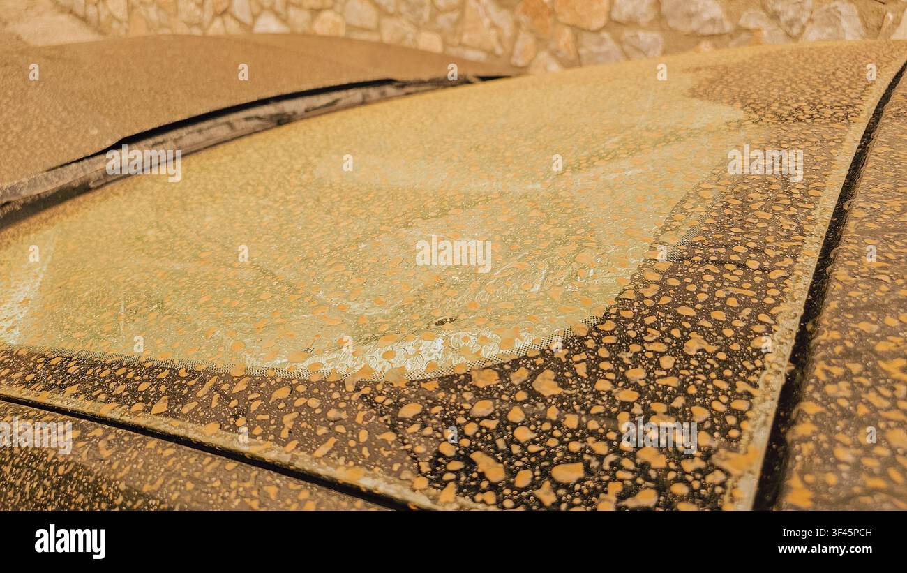 Nahaufnahme einer Autowindschutzscheibe, bedeckt mit orangefarbenem afrikanischem Saharastaub und getrockneten Regentropfen nach einem schweren Sandsturm in Kreta, Griechenland, für apokalyptisches Wettermaterial Stockfoto