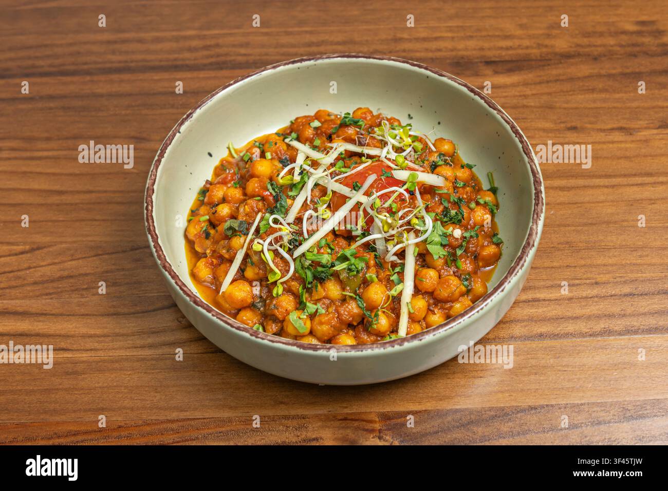 Chana Masala Kichererbsen-Curry garniert mit Sprossen und julienierten Gemüsen in einer rustikalen Schüssel Stockfoto