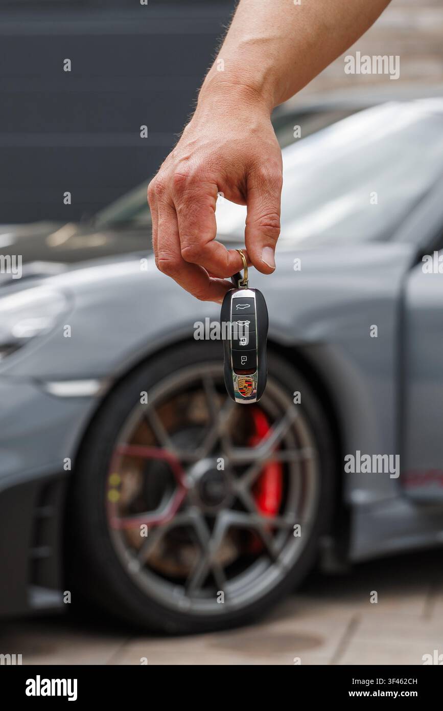 Ljubljana, Slowenien - 18. Mai 2026: Eine Hand hält einen Porsche GT4 RS-Schlüssel, während sie vor dem Luxus-Sportwagen steht. Die Szene zeigt Autobesitz Stockfoto