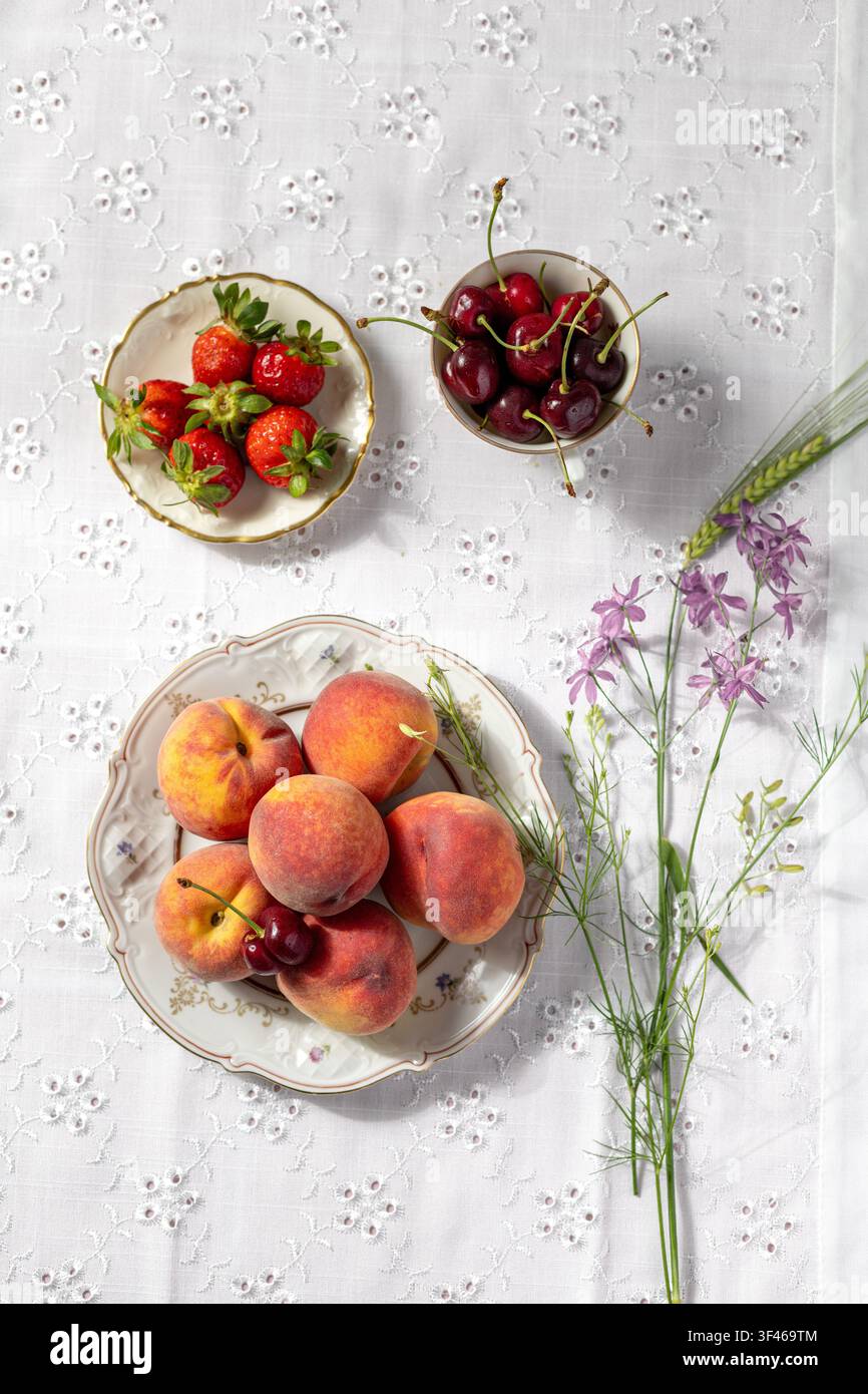Frische Sommerfrüchte und Blumen auf Spitzentischdecke Stockfoto