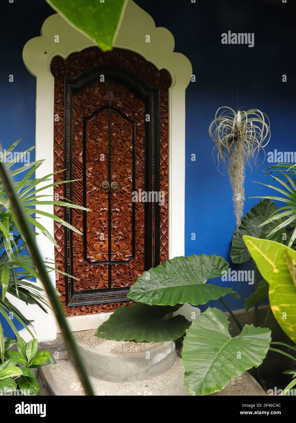 Einladende, wunderschön handgefertigte geschnitzte Holztür im mystischen Bali. Helles blaues Indigo-Haus in Ubud Stockfoto
